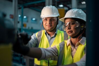 Technicains in yellow jackets, goggles and hard hats accessing something off screen