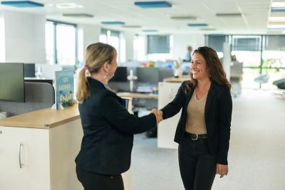 Two formally dressed women shaking hands in an office.