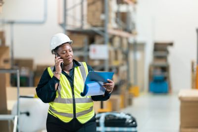 A woman engineer holding and reading a document on a factory floor.