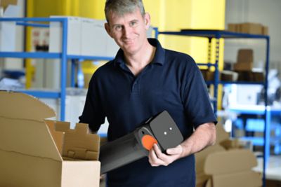 A man in a warehouse holds a filter model in his hands, ready to place into the box next to him