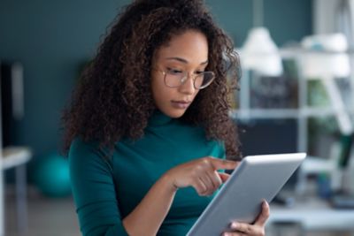 Portrait of concentrated young entrepreneur woman using her digital tablet while standing in the office.